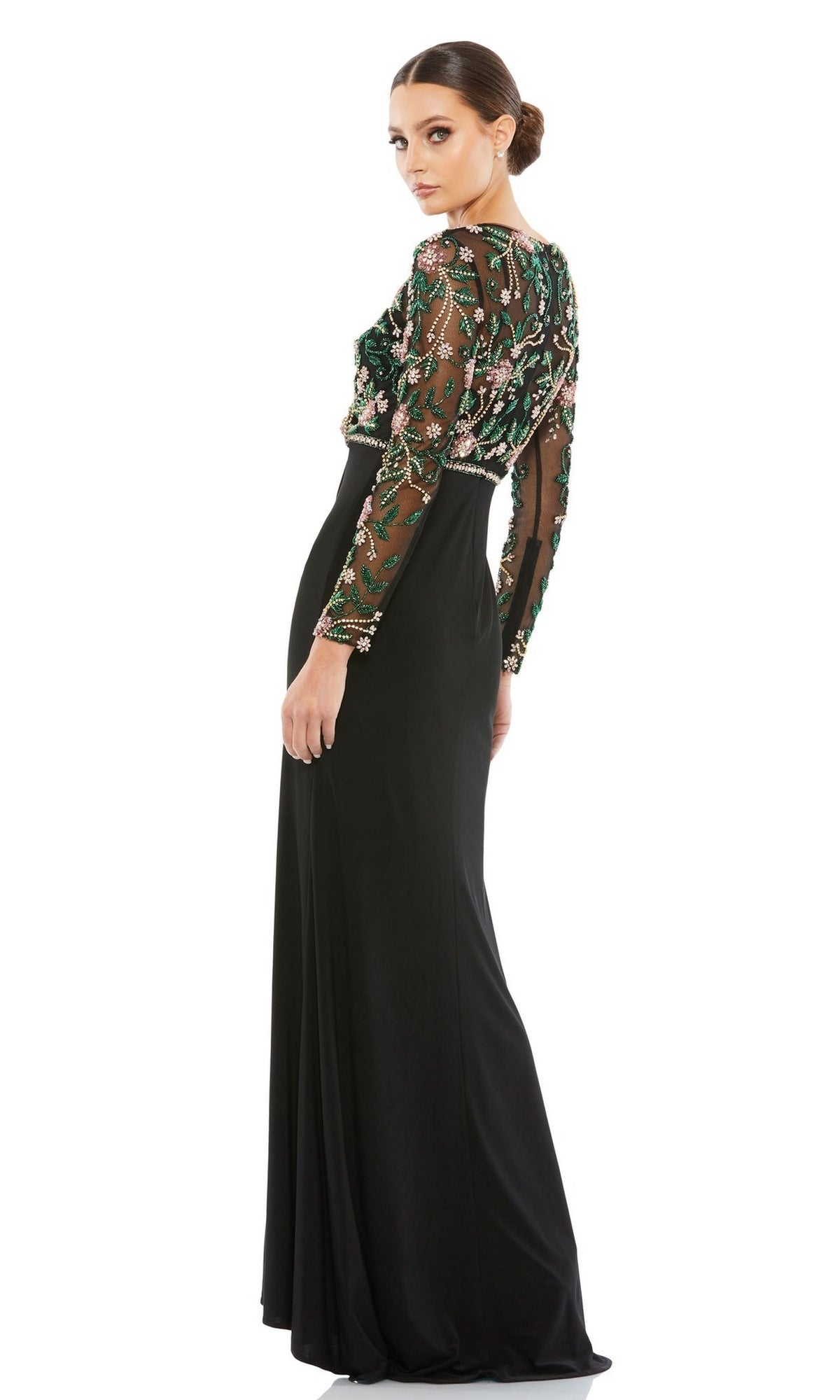 A woman stands against a white background, looking over her shoulder in the Mac Duggal 67870 long sleeve black formal dress featuring a beaded bodice and sheer embroidered floral top.